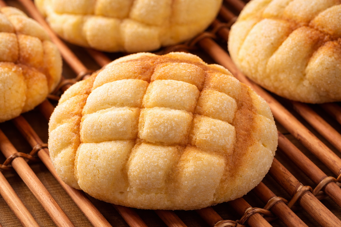 Golden Japanese melon pan sweet bread with a crunchy sugar cookie crust and classic melon pattern, cooling on a bamboo rack in a bakery setting.